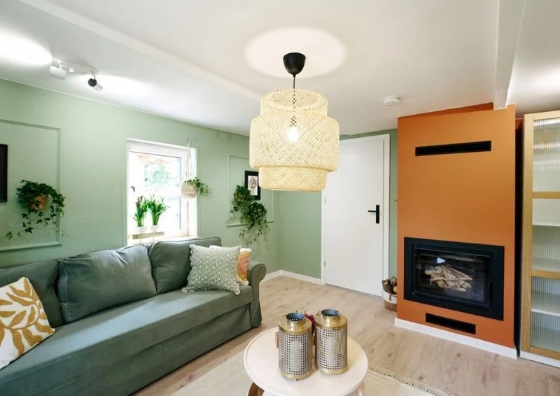Pomarańczowy kominek kontrastuje z zielonymi ścianami i dodatkami