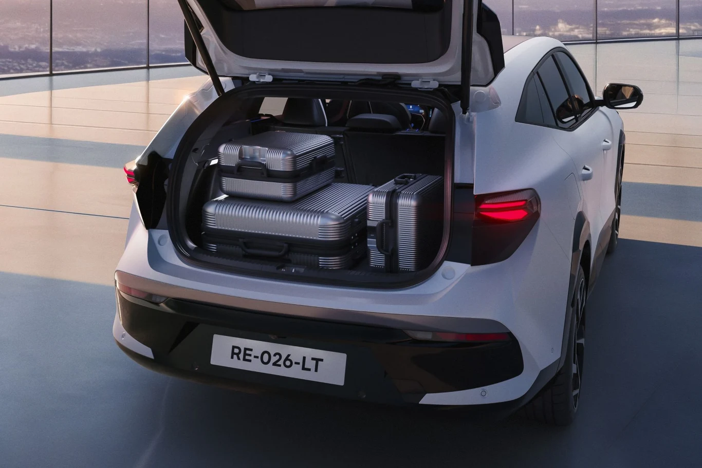 Białe auto typu SUV z otwartym bagażnikiem, w którym znajdują się trzy nowoczesne, metalowe walizki. Samochód stoi na jasnym, przestronnym placu z dużymi oknami w tle.