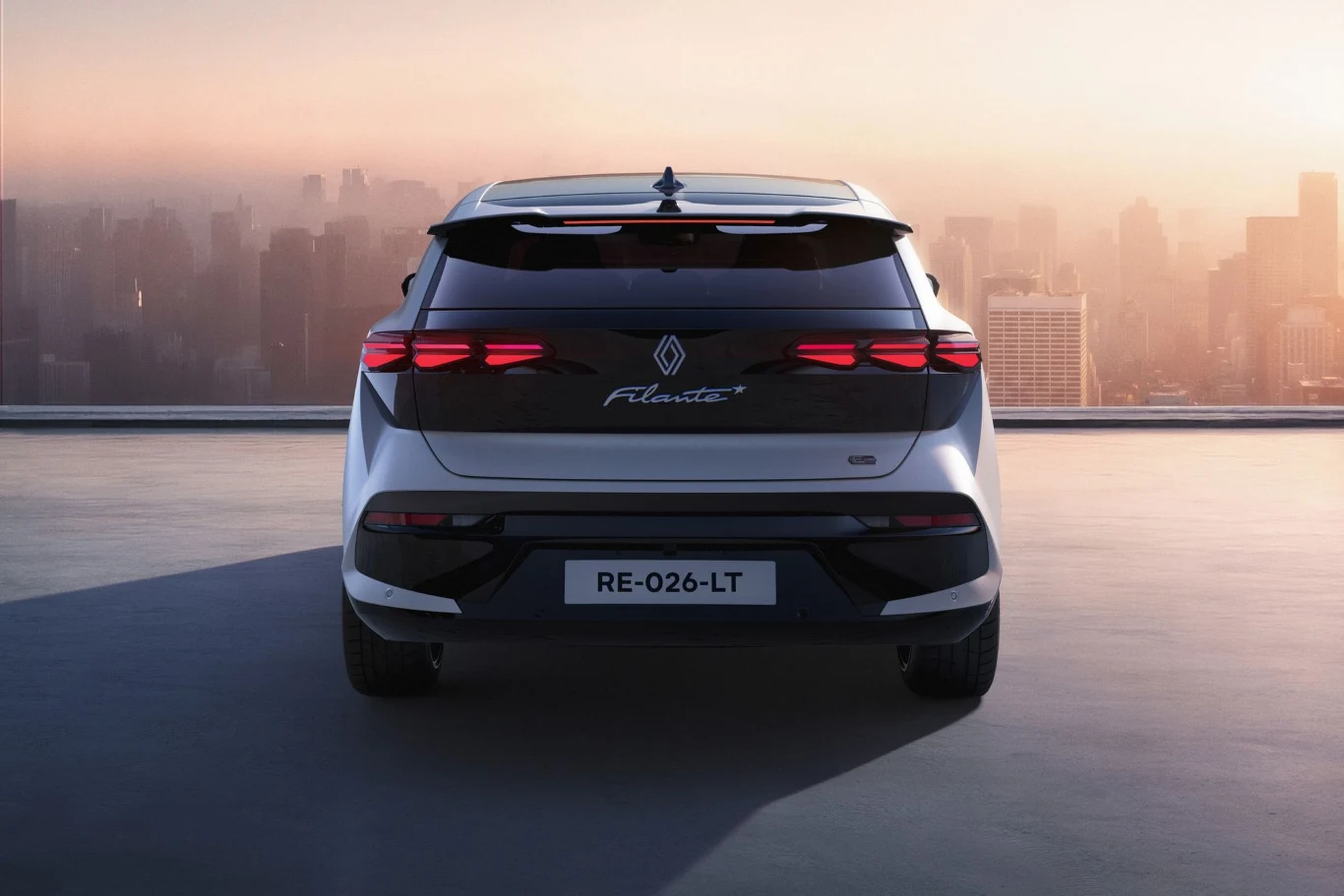 Nowoczesny samochód osobowy marki Renault, widziany od tyłu, zaparkowany na płaskiej powierzchni przy panoramie miejskiej w świetle zachodzącego słońca.