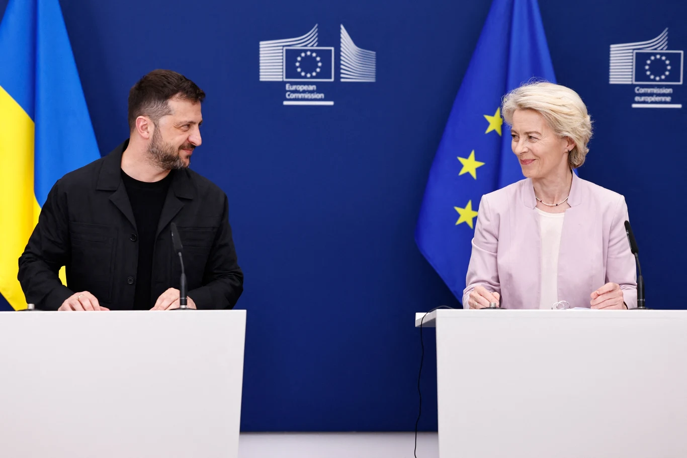 Ursula von der Leyen proponuje pożyczki Ukrainie Dwójka polityków stoi przy mównicach, za nimi flagi Unii Europejskiej i Ukrainy oraz logo Komisji Europejskiej, oboje patrzą na siebie i uśmiechają się podczas konferencji prasowej.