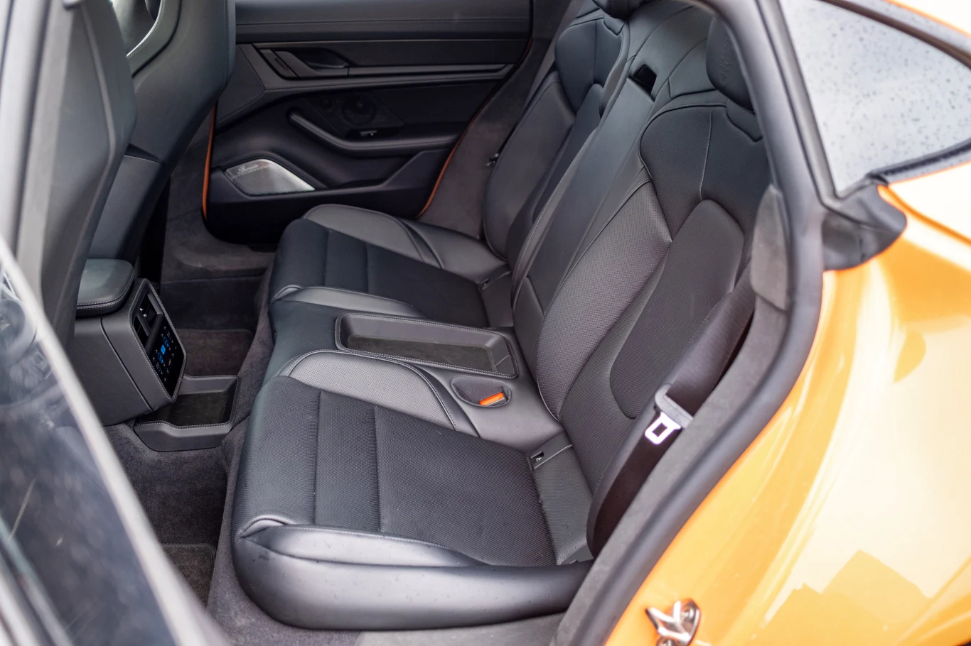 Tylny rząd siedzeń samochodu o nowoczesnym wykończeniu, skórzane fotele z widocznym podłokietnikiem, panele drzwiowe z detalami oraz centralna konsola z wentylacją.