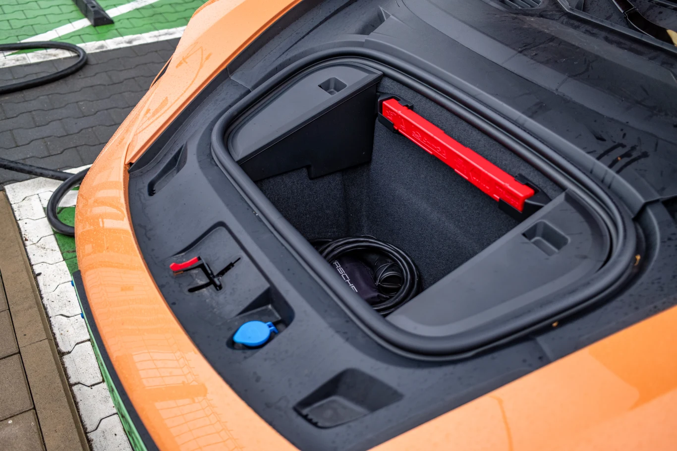 Przedni bagażnik auta elektrycznego, w którym znajdują się elementy wyposażenia takie jak kabel do ładowania oraz trójkąt ostrzegawczy.