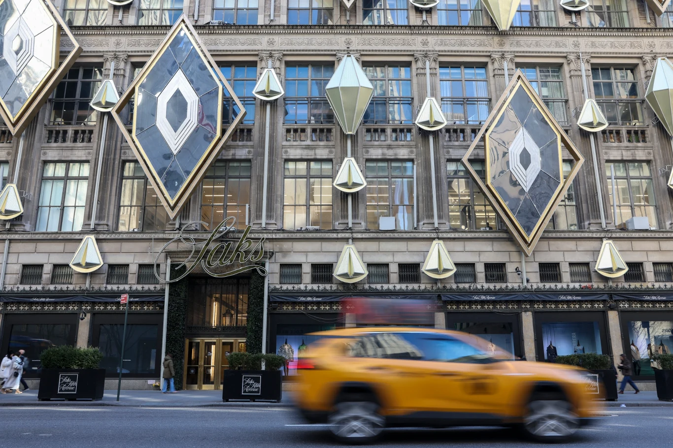 Sklep Saks Fifth Avenue w Nowym Jorku. Spółka matka (Saks Global) mierzy się z niewypłacalnością Fasada eleganckiego wielopiętrowego budynku ozdobiona dużymi, geometrycznymi dekoracjami w kształcie diamentów, na pierwszym planie żółta nowojorska taksówka w ruchu.