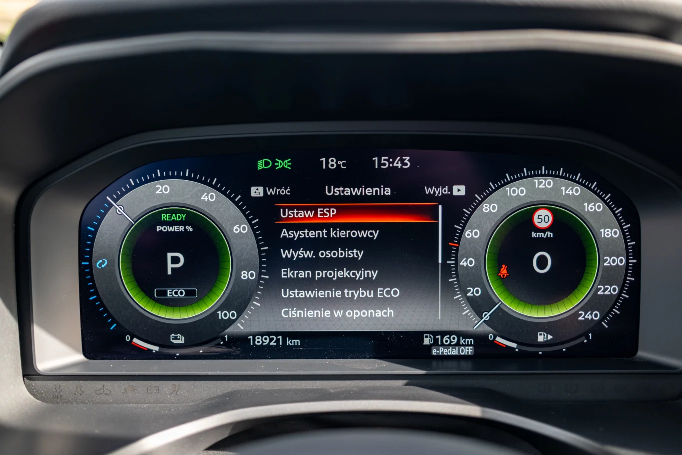 Cyfrowy zestaw wskaźników samochodu z czytelnymi zegarami, wskazówkami dotyczącymi jazdy, ustawieniami systemów wspomagających oraz informacjami o aktualnym przebiegu, temperaturze zewnętrznej i zasięgu.
