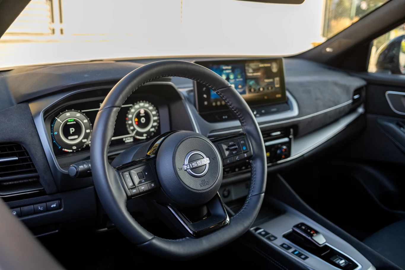 Nowoczesna deska rozdzielcza samochodu Nissan z cyfrowymi zegarami, dużym dotykowym ekranem na środku, wielofunkcyjną kierownicą i centralną konsolą z elektronicznym panelem sterowania.