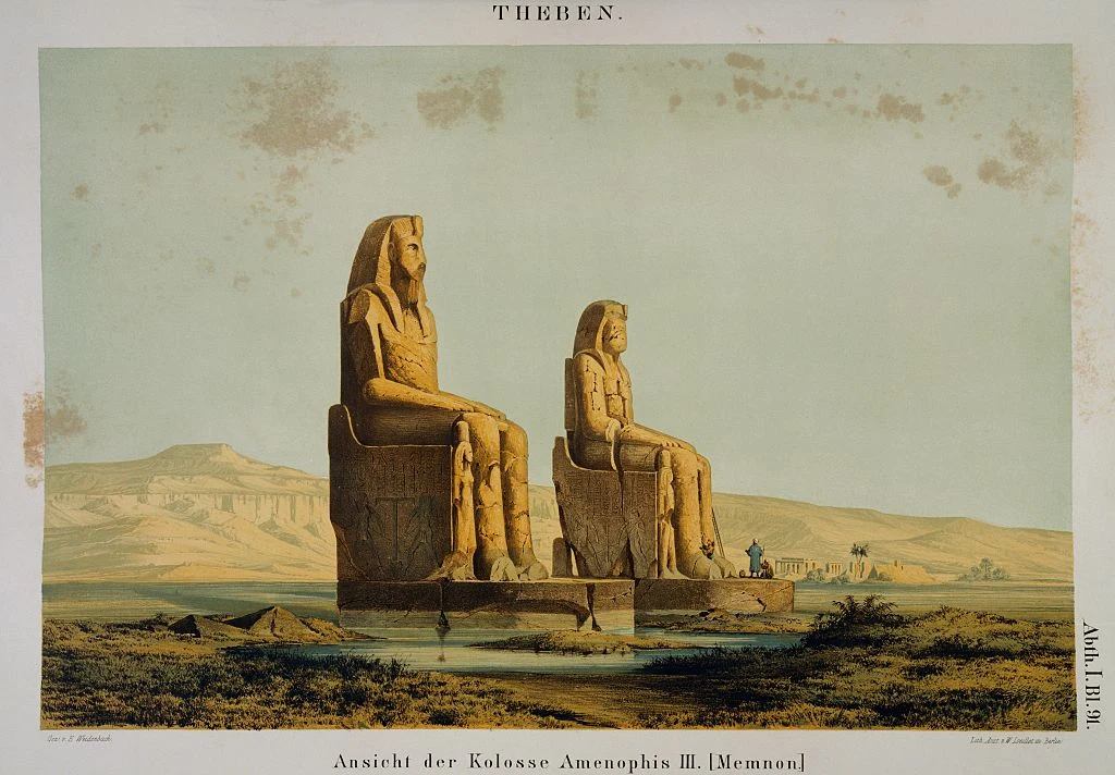 Dwa monumentalne posągi siedzących postaci wykonane z kamienia, ustawione na prostokątnej platformie, umieszczone na pustynnej równinie z dalekim widokiem na górzysty krajobraz w tle.