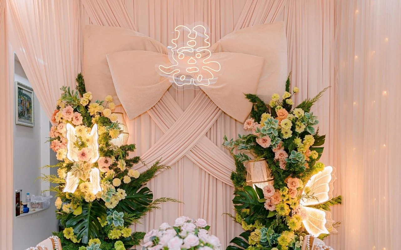 Elegancka dekoracja ślubna z przewagą jasnych tkanin i kokardą, podświetlany chiński znak szczęścia, bogate kompozycje kwiatowe i zielone liście z elementami świetlnymi.