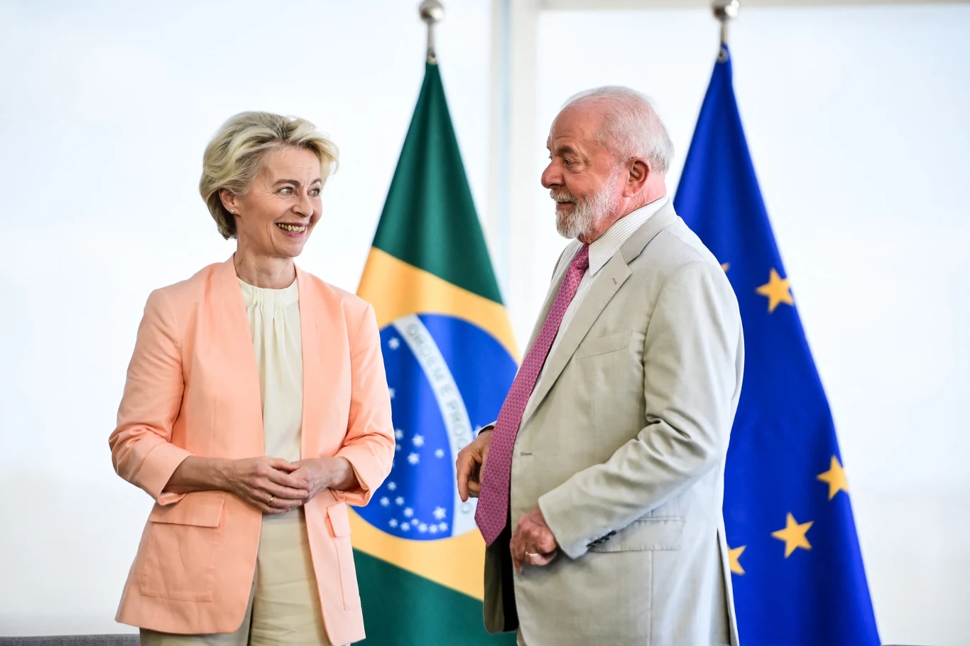 Zapadła decyzja w sprawie Mercosur. KE wdroży porozumienie Dwie osoby w eleganckich garniturach prowadzą rozmowę na tle flag Brazylii i Unii Europejskiej. Osoby wyglądają na zadowolone, przyjazna atmosfera.