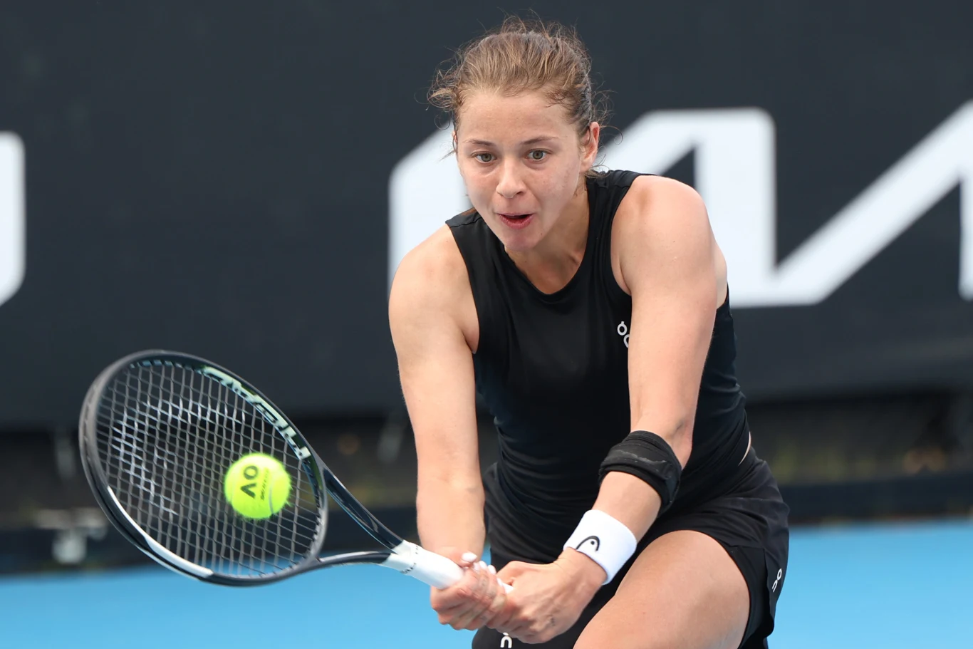 Kobieta w czarnej sportowej koszulce podczas gry w tenisa, skoncentrowana na odbiciu piłki rakietą na korcie tenisowym.