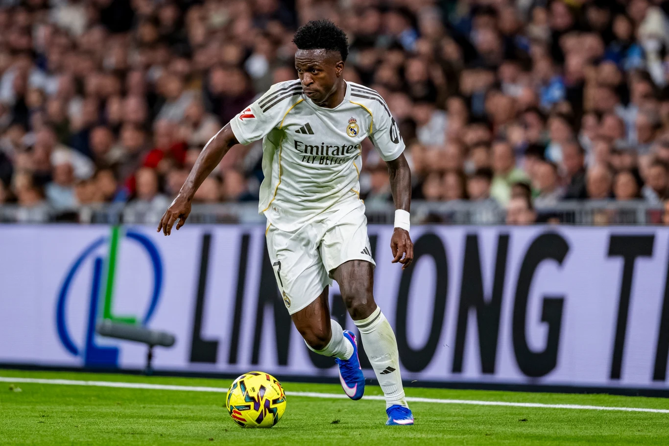 Vinicius Junior w barwach Realu Madryt podczas meczu La Liga w sezonie 2025/2026 Piłkarz Realu Madryt w białym stroju prowadzi piłkę podczas meczu na stadionie, w tle widoczna pełna trybuna kibiców.