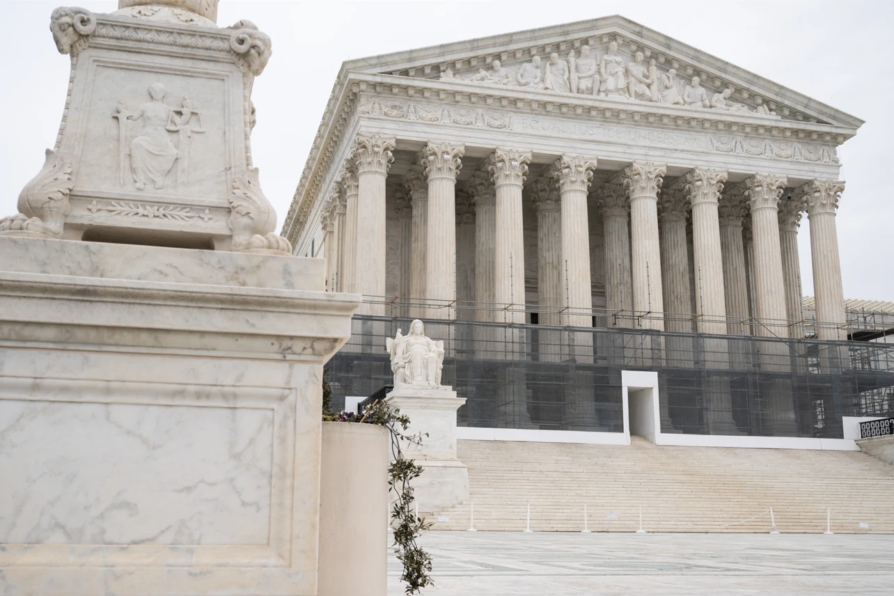 Monumentalny budynek z kolumnadą i szerokimi schodami stanowiący siedzibę sądu najwyższego, na pierwszym planie element marmurowego pomnika z płaskorzeźbą.