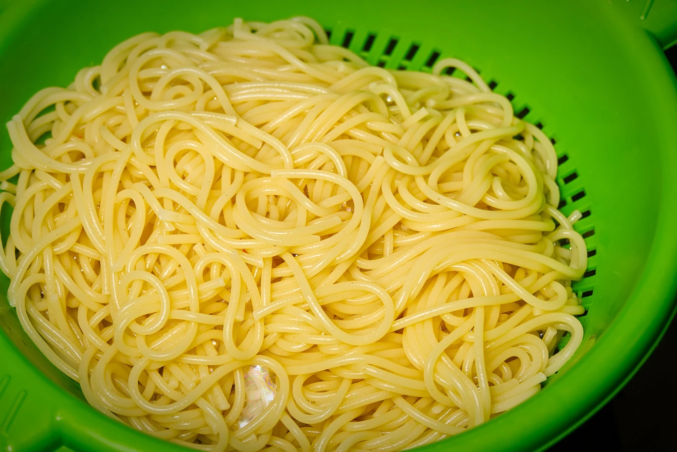 Świeżo ugotowany makaron spaghetti odsączony w zielonym durszlaku, widoczne sprężyste nitki makaronu gotowe do podania