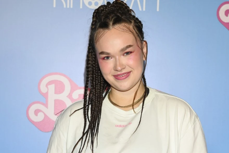 Anastazja Maciąg zgłosiła się do eurowizyjnych preselekcji z piosenką "Wild Child" Młoda kobieta o jasnej karnacji i afrykańskich warkoczykach, z delikatnym makijażem, uśmiechnięta, ubrana w białą koszulkę, pozująca na tle niebieskiej ścianki z logo Barbie.