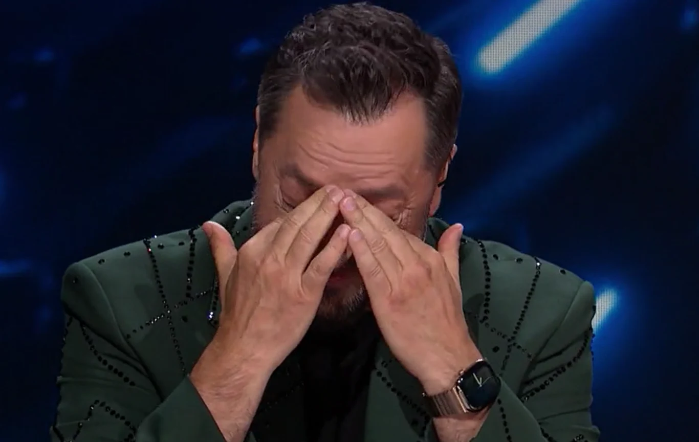 Marcin Miller w "Disco Star" nie krył łez wzruszenia Mężczyzna w zielonej marynarce zakrywający twarz dłońmi w geście silnej emocji, siedzący na tle niebieskich świateł.