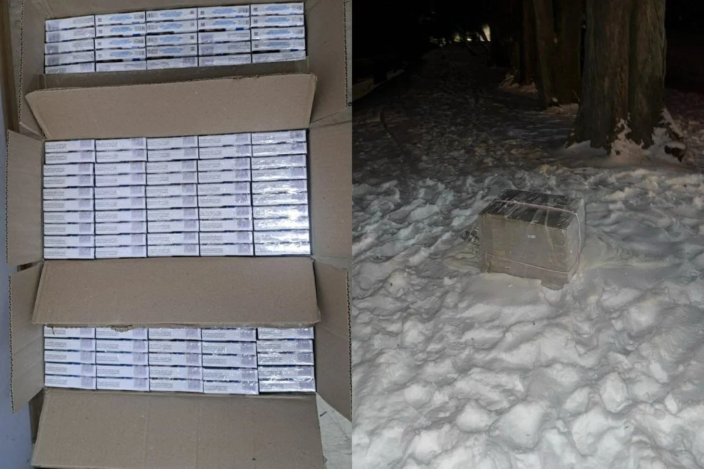 Podlaska policja zabezpieczyła dwa balony przemytnicze Karton wypełniony licznymi paczkami papierosów, obok na śniegu porzucona paczka podobnych rozmiarów, w tle drzewa i ciemność nocy.