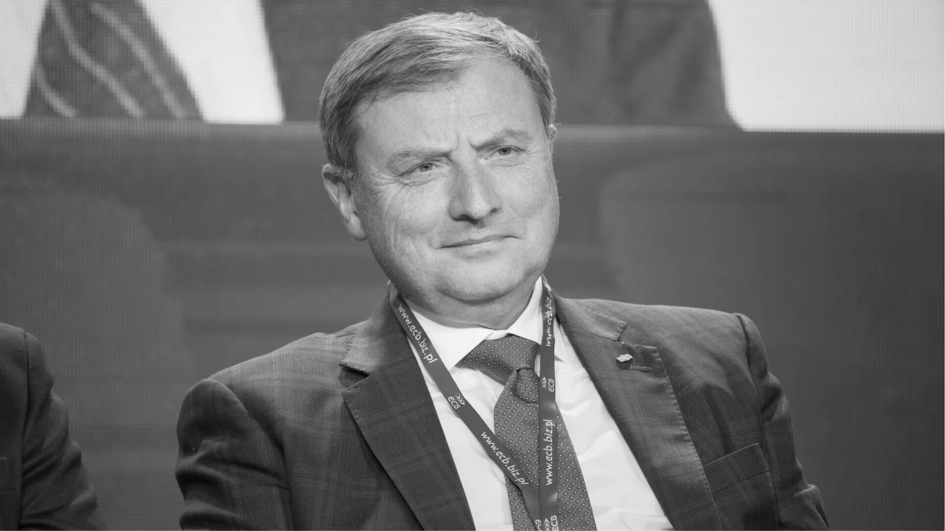 Wojciech Hann nie żyje. Miał 61 lat Mężczyzna w średnim wieku w garniturze i krawacie, siedzi z poważnym wyrazem twarzy, ma przypięty identyfikator na smyczy, w tle widoczna niewyraźna sylwetka innej osoby.