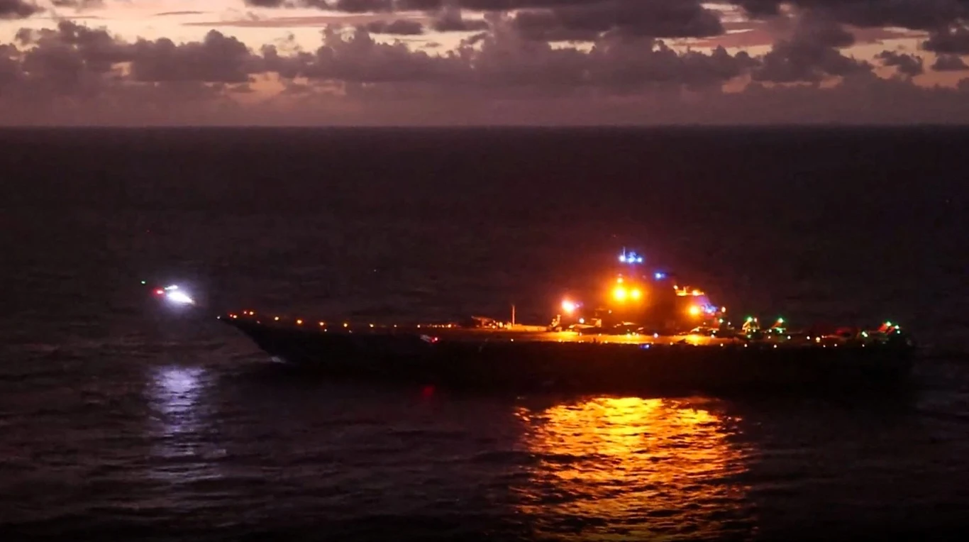 Myśliwiec startujący z chińskiego lotniskowca Liaoning na wschód od Tajwanu (zdjęcie ilustracyjne) Okręt wojskowy oświetlony licznymi światłami na otwartym morzu nocą, w pobliżu na wodzie znajduje się mały pojazd lub łódź z jasnym światłem, w tle ciemne niebo z chmurami oraz lekko rozjaśniony horyzont.