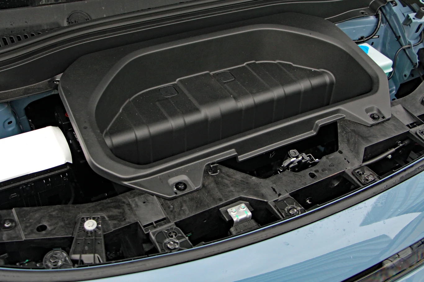 Przedni bagażnik samochodu elektrycznego z dużą, plastikową komorą przechowywania i widocznymi elementami technicznymi pod maską.