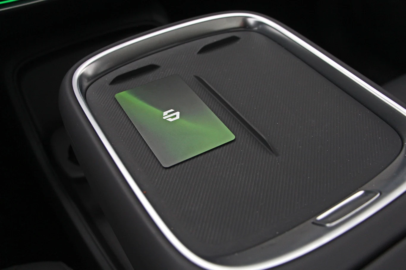 Czarny schowek lub miejsce na desce rozdzielczej nowoczesnego samochodu z zieloną kartą o błyszczącej powierzchni i widocznym białym logo pośrodku.