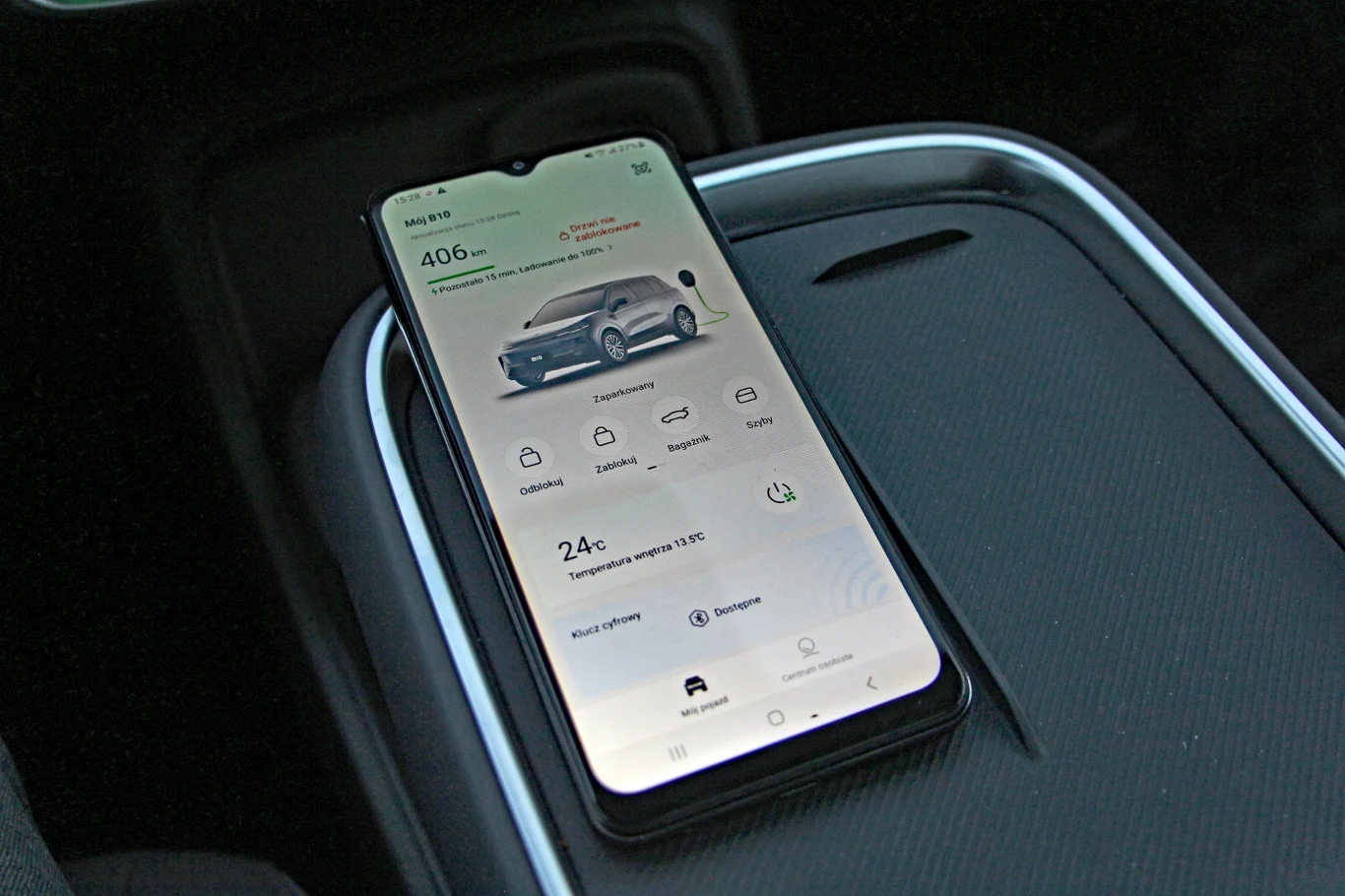 Nowoczesny smartfon leżący na konsoli samochodowej z uruchomioną aplikacją umożliwiającą kontrolę pojazdu elektrycznego, wyświetlającą informacje o zasięgu, stanie klimatyzacji oraz inne funkcje związane z autem.