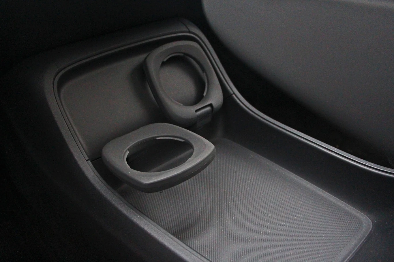 Wnętrze samochodu z dwoma uchwytami na napoje umieszczonymi obok siebie, wykonanymi z ciemnego plastiku, zlokalizowanymi pomiędzy siedzeniami.