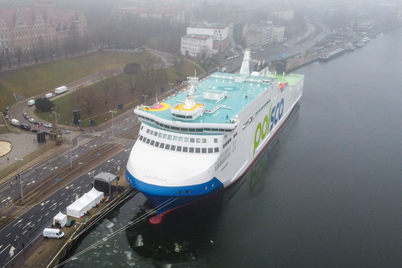 Szczecin. Nowy prom "Jantar" został zaprezentowany przy Wałach Chrobrego Duży nowoczesny prom pasażersko-towarowy firmy Polferries zacumowany przy nabrzeżu, otoczony infrastrukturą portową oraz zabudowaniami miejskimi, widok z lotu ptaka w pochmurny, mglisty dzień.