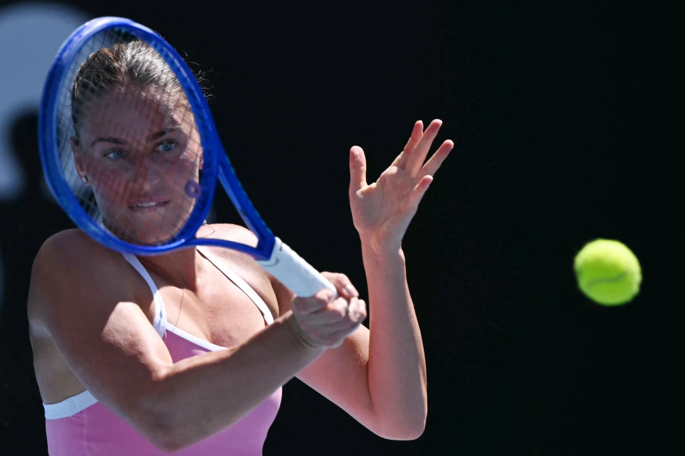 Zawodniczka podczas intensywnego meczu tenisowego skoncentrowana na odbiciu nadlatującej piłki, w tle ciemne tło podkreślające dynamikę akcji.