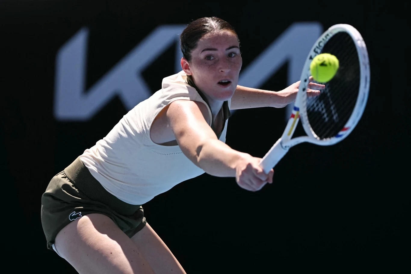 Tenisistka koncentrująca się na uderzeniu piłki rakietą w trakcie meczu, dynamiczna poza, sportowa odzież, żółta piłka w powietrzu, rozmyte tło kortu.