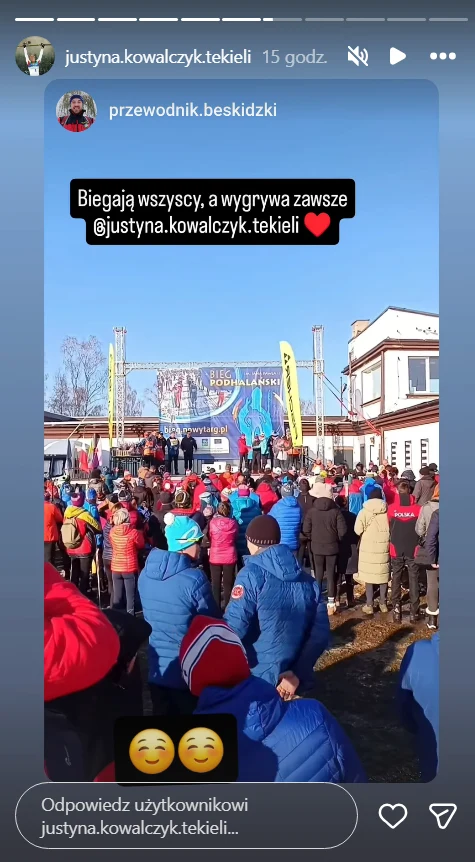 Justyna Kowalczyk-Tekieli wygrała w Biegu Podhalańskim Tłum ludzi zgromadzony przed sceną na otwartej przestrzeni, liczne kolorowe ubrania, transparenty i flagi związane z zawodami sportowymi, słoneczna pogoda, budynki po obu stronach placu, na scenie widoczny duży baner z sylwetką sportowca.