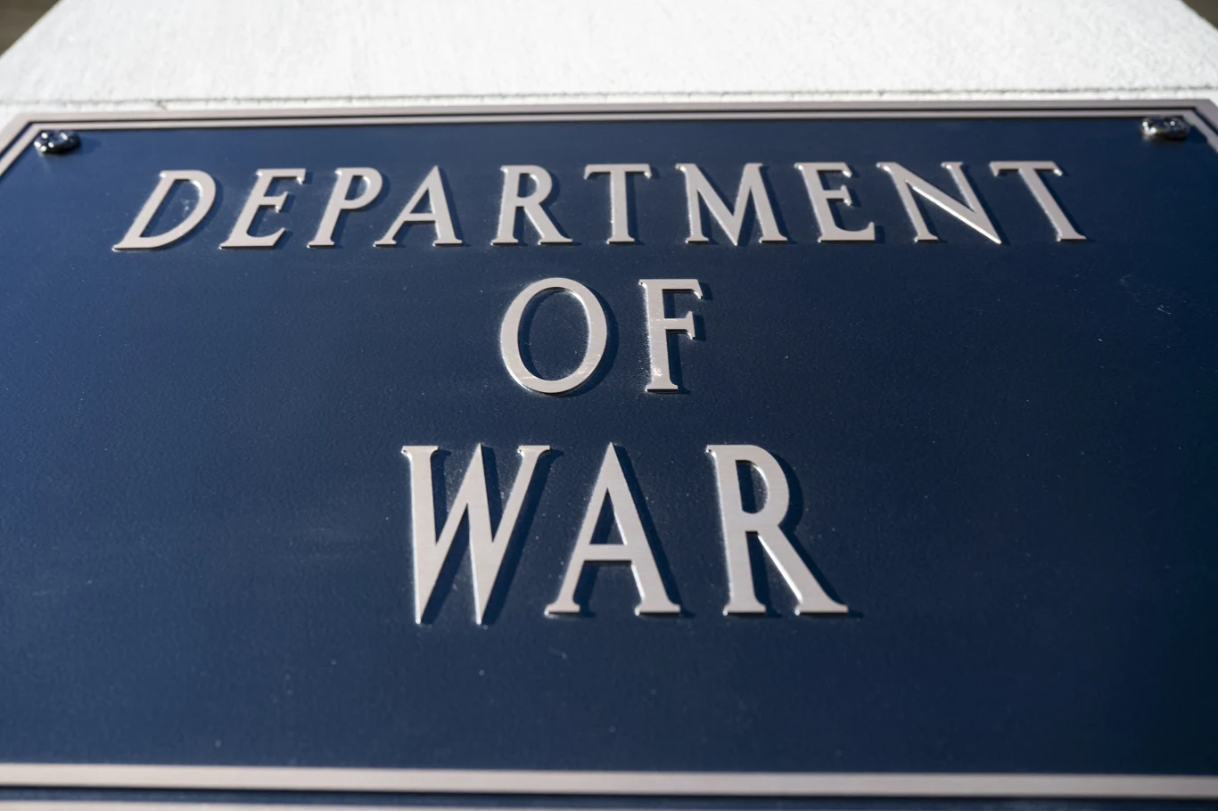 Metalowa tablica z napisem "Department of War" na tle jasnej powierzchni.