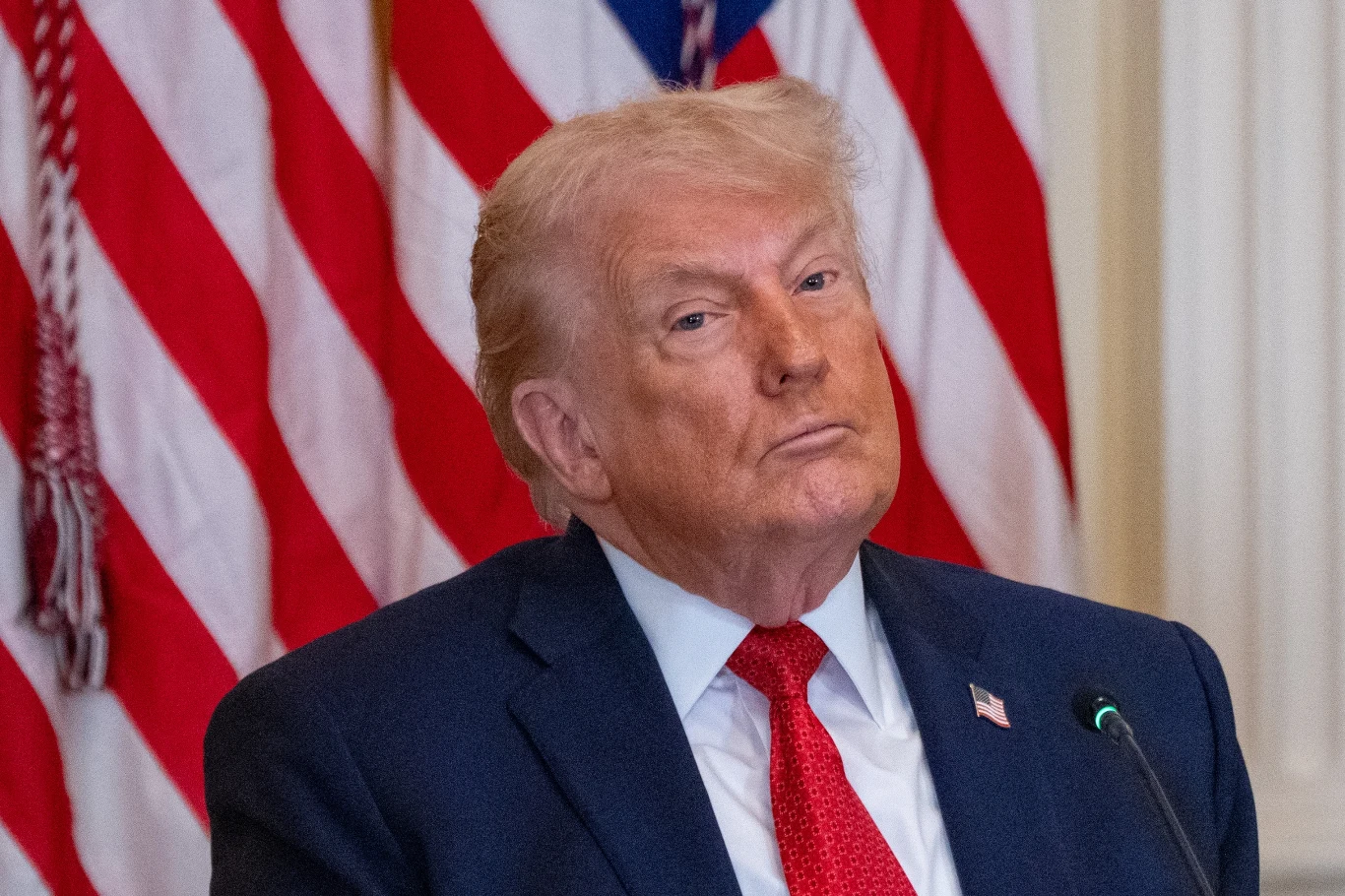 Od poniedziałku importerzy mogą domagać się od USA zwrotu pieniędzy za nadpłacone cła. Ruszyło składanie wniosków Donald Trump w garniturze i czerwonym krawacie przy mikrofonie na tle flag USA.