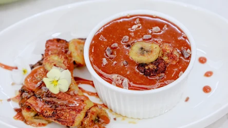 Biała kokilka z miniserniczkiem polanym sosem karmelowym, obok smażone banany i kwiat.