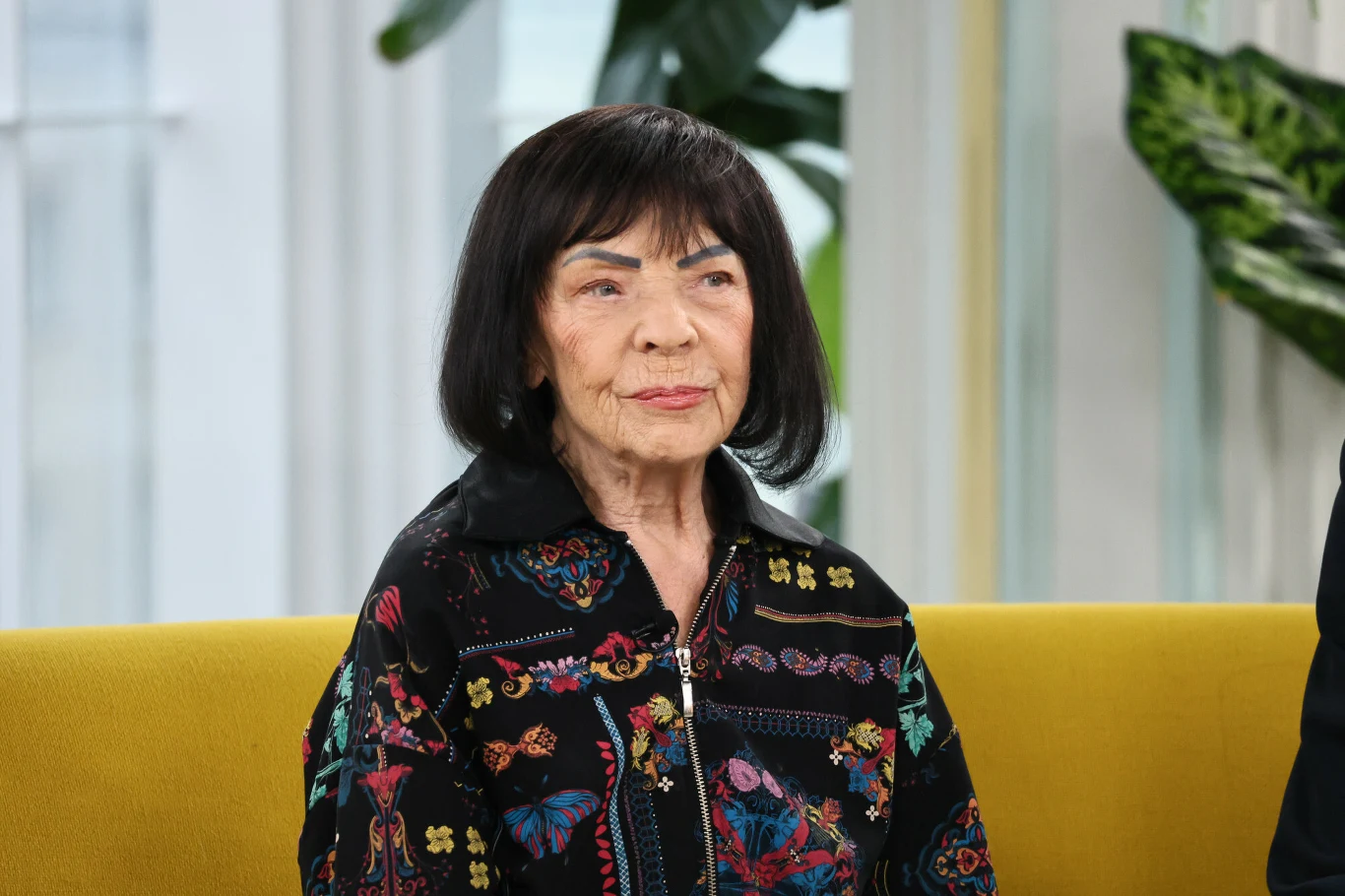 Sława Przybylska pokazała zdjęcie z Katarzyną Gärtner Starsza kobieta o ciemnych, prostych włosach siedzi na żółtej sofie. Ubrana jest w ciemną, wzorzystą kurtkę, a w tle widoczna jest jasna przestrzeń z roślinami i dużymi oknami.