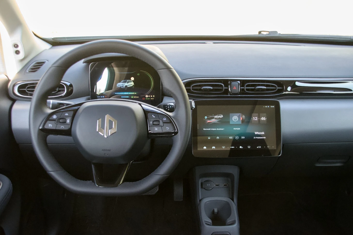 Nowoczesna deska rozdzielcza samochodu elektrycznego z centralnym ekranem dotykowym, cyfrowym zestawem wskaźników oraz kierownicą z wieloma przyciskami funkcyjnymi.