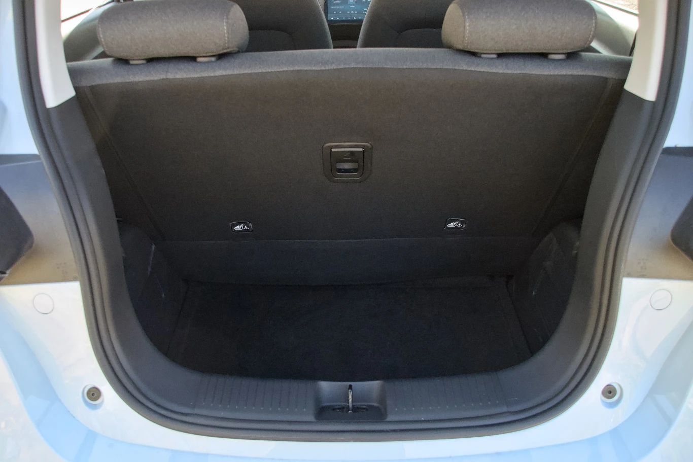 Otwarty bagażnik samochodu z widocznym tylnym oparciem kanapy, wnętrze czyste i puste, w tle fragmenty tylnych zagłówków.