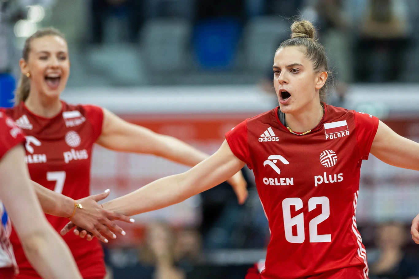 Julia Nowicka w reprezentacji Polski Polskie siatkarki w czerwonych strojach świętują zdobycie punktu podczas meczu, w tle widać rozmyte trybuny i innych zawodników.