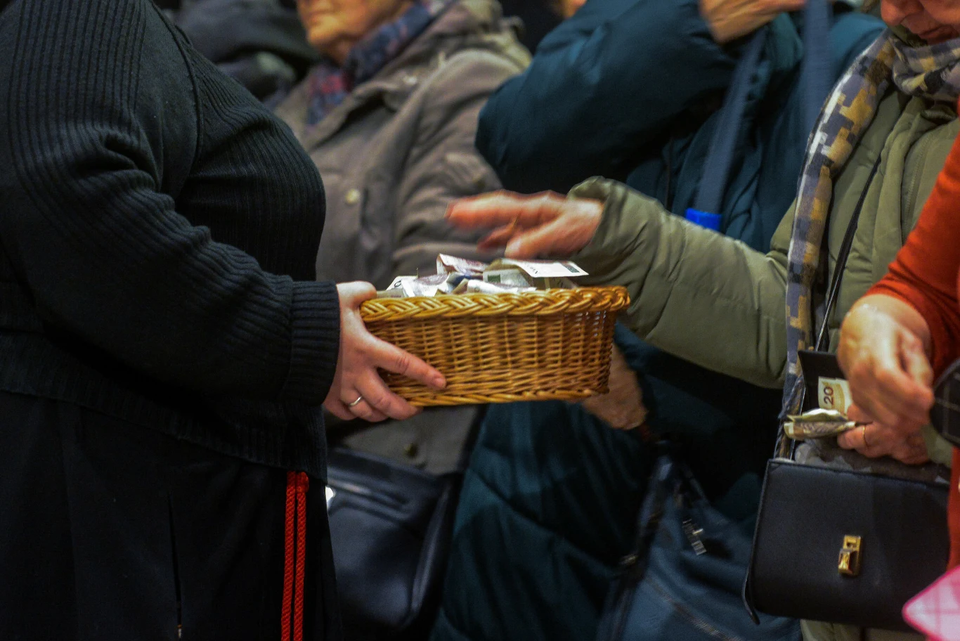 Wielu duchownych rozlicza się z wiernymi z "co łaska". Koszyk wypełniony banknotami i monetami podawany przez osobę w czarnej odzieży, do koszyka wkładają pieniądze osoby w kurtkach, wokół zgromadzeni ludzie w zimowych ubraniach.