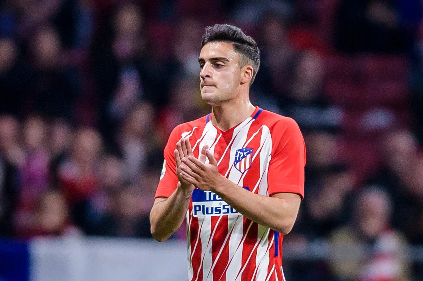 Piłkarz w czerwono-białej koszulce Atletico Madryt stoi na boisku i klaszcze, będąc w centrum zainteresowania, z rozmytym tłem trybun oraz publicznością.