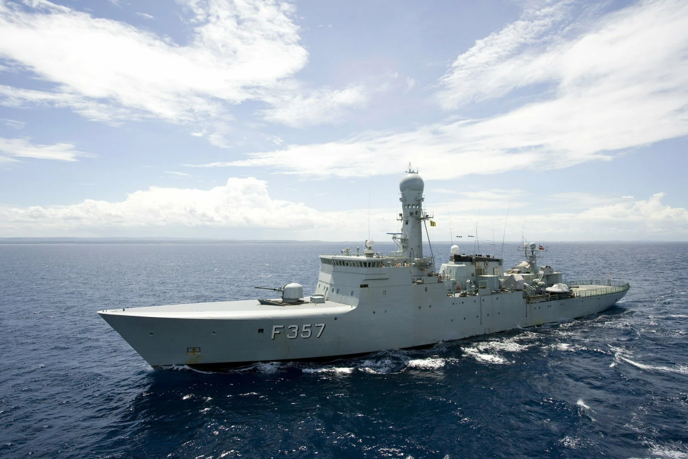 Duży okręt wojenny z numerem F357 płynie po wodach oceanu pod niebem z lekkimi chmurami, na pokładzie widoczne są radary i uzbrojenie.