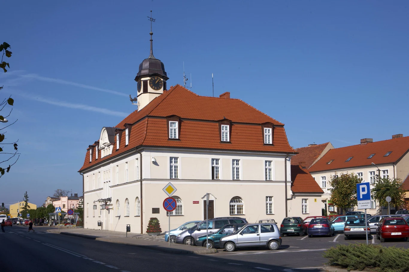 Ratusz z czasów Teofili strawił pożar, a na jego miejscu wzniesiono nową neobarokową budowlę Zabytkowy ratusz pokryty czerwoną dachówką z niewielką wieżą i zegarem, otoczony zaparkowanymi samochodami, przy ulicy z wyraźnie widocznymi znakami drogowymi, w tle inne budynki mieszkalne.