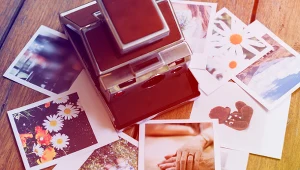 Aparat typu Polaroid pośród odbitek rozrzuconych na drewnianym stole