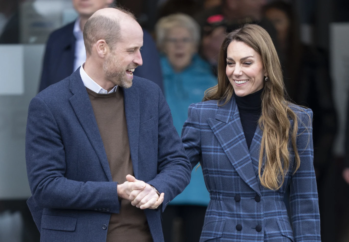 Księżna Kate tryskała doskonałym humorem tego dnia Uśmiechnięta para ubrana elegancko rozmawia ze sobą, stojąc obok siebie w otoczeniu ludzi w tle, dominują neutralne kolory ubrań i delikatna gestykulacja.