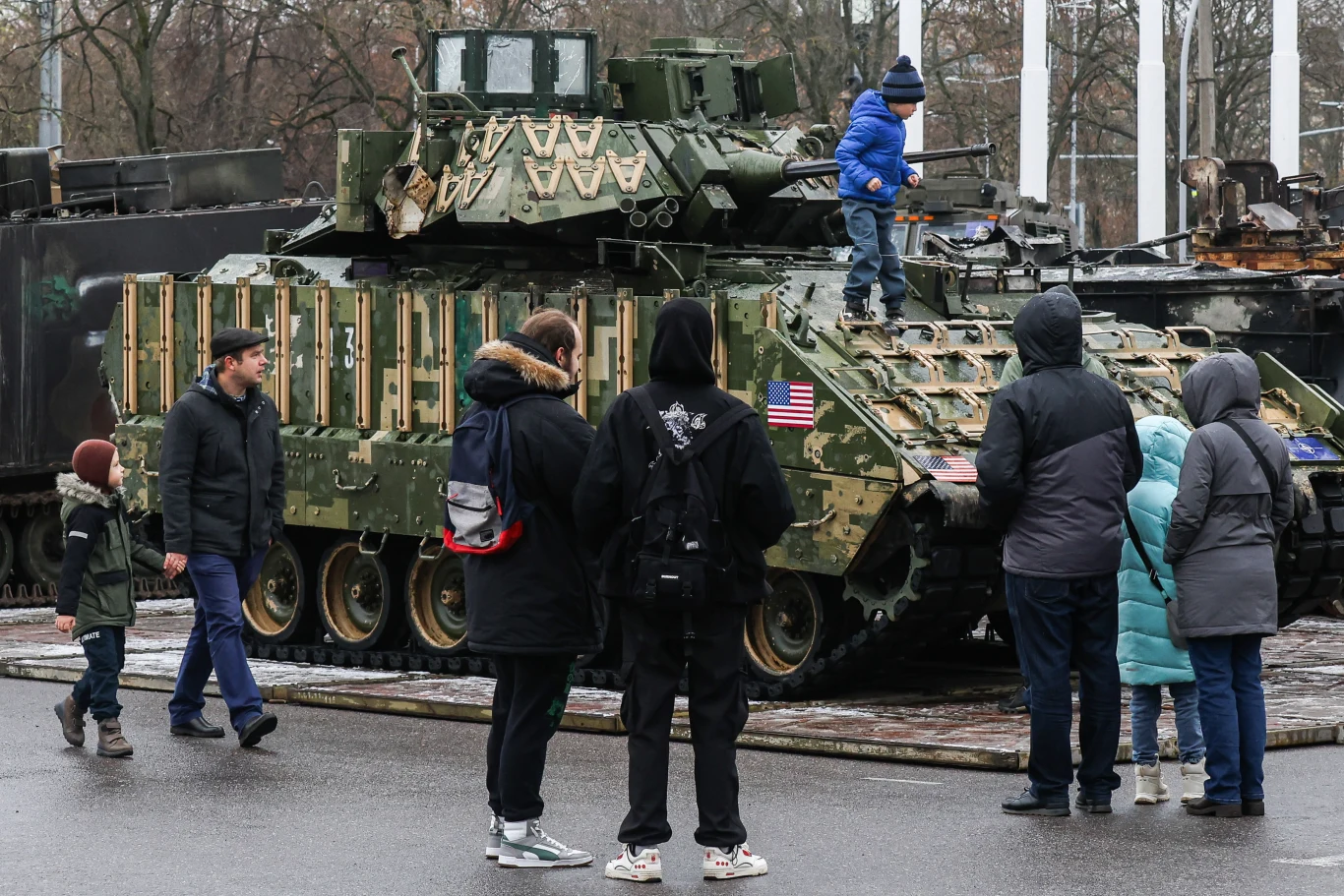Jedna z wielu wystaw wojskowych organizowanych przez Rosję. Petersburg, 03.11.2024 (zdj. poglądowe) Grupa ludzi, w tym dzieci i dorośli, ogląda amerykański pojazd opancerzony ustawiony na terenie miejskim, jedno z dzieci wspina się na pojazd, całość odbywa się w spokojnej atmosferze, wokół zimowa aura i drzewa bez liści.