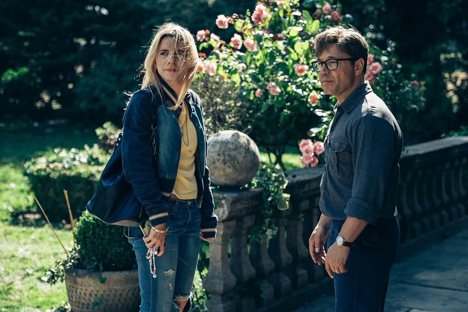 Nagrodzony Złotym Globem Stephen Graham gra główną rolę w nowym filmie Jana Komasy "Dobry chłopiec" Kobieta w jasnej bluzie oraz mężczyzna w okularach stoją razem na tle ogrodu z kwitnącymi różami oraz kamienną balustradą, światło słoneczne rozświetla scenę i podkreśla letnią atmosferę.