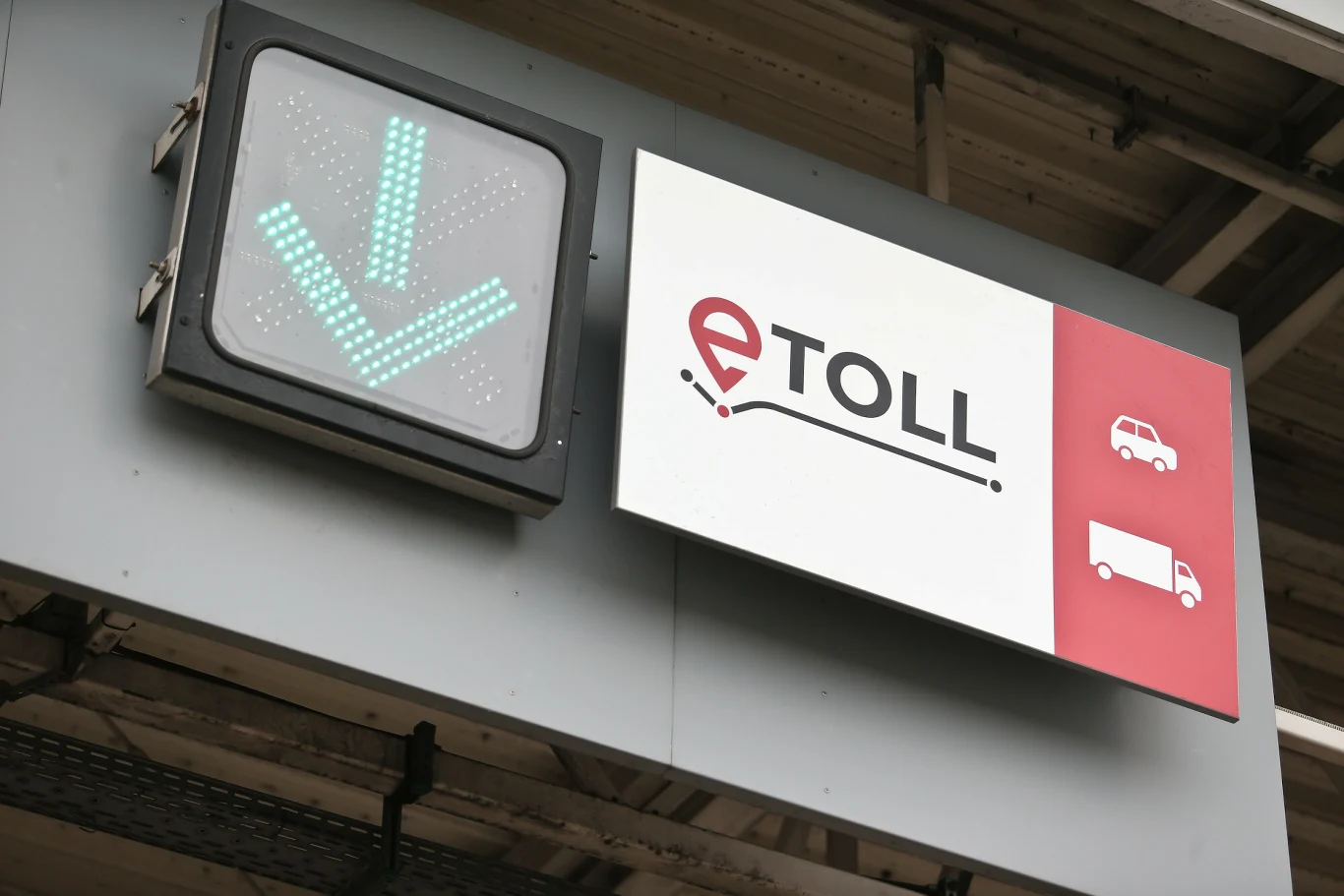 Od lutego więcej płatnych dróg w Polsce. Przejazdy e-TOLL drożeją Elektroniczny znak informacyjny z zieloną strzałką skierowaną w dół oraz tablica z logo systemu eTOLL i piktogramami samochodu osobowego i ciężarówki zamontowane pod dachem w punkcie poboru opłat.