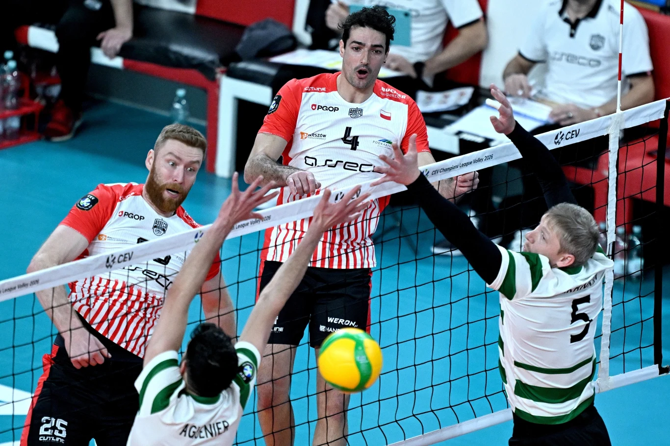 Siatkarze walczący o punkt podczas meczu, zawodnik drużyny w czerwono-białych koszulkach szykuje się do ataku, podczas gdy zawodnik w zielono-białym stroju wykonuje blok.