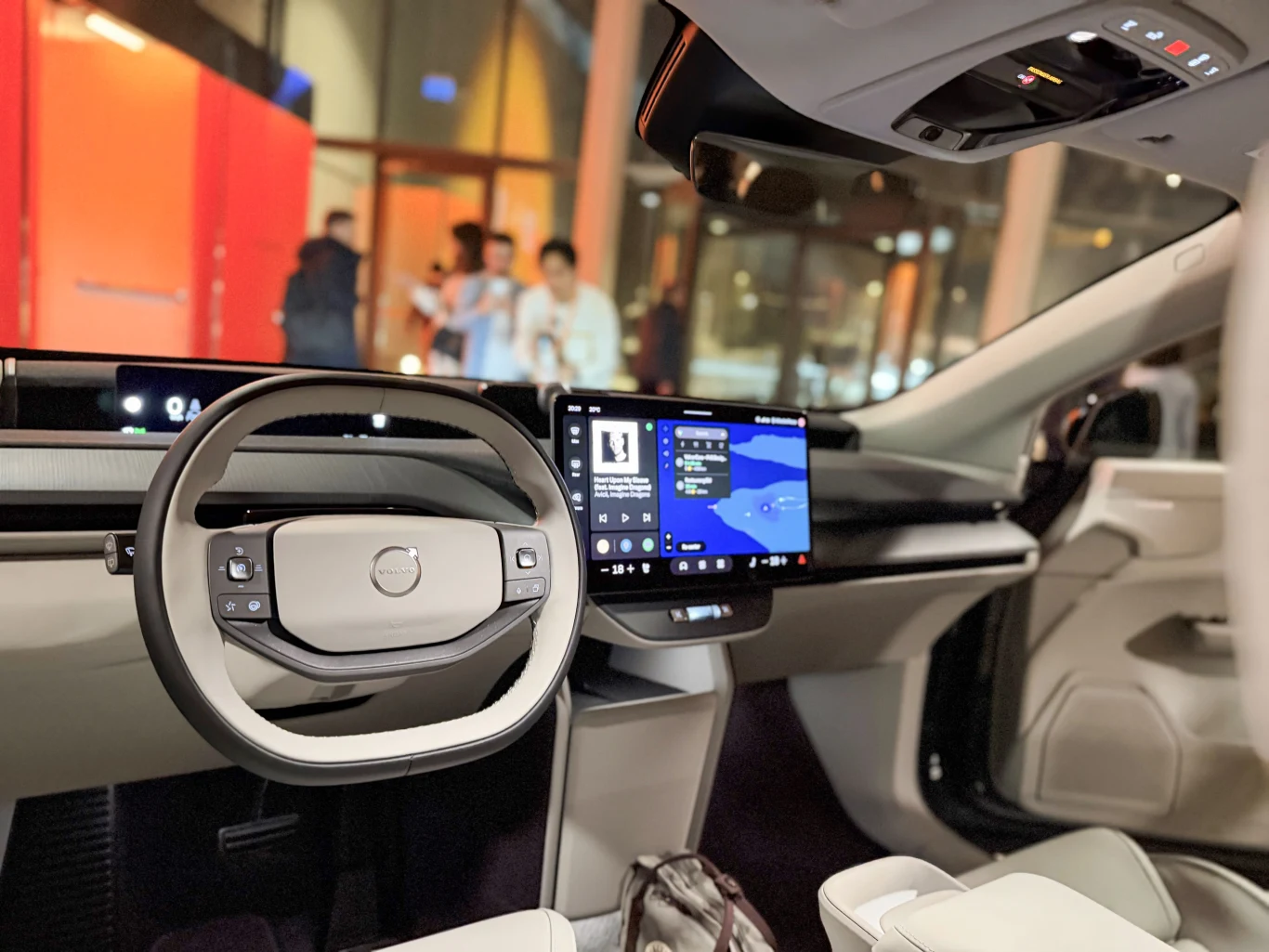 Nowoczesne wnętrze samochodu elektrycznego Volvo z widocznym cyfrowym panelem sterowania, dużym ekranem dotykowym na konsoli centralnej i designerską kierownicą, jasne wykończenie foteli oraz elementów kokpitu podkreśla technologiczny charakter auta.