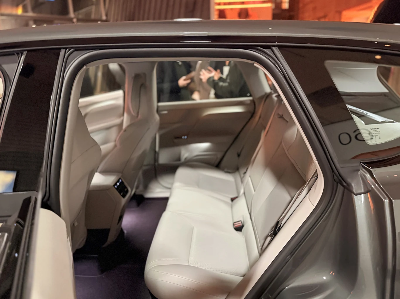 Luksusowe, jasne wnętrze tylnej części samochodu z wygodną, skórzaną kanapą oraz nowoczesnym panelem sterowania widocznym na podłokietniku. Jasne wykończenie nadaje wnętrzu elegancki i przestronny charakter.