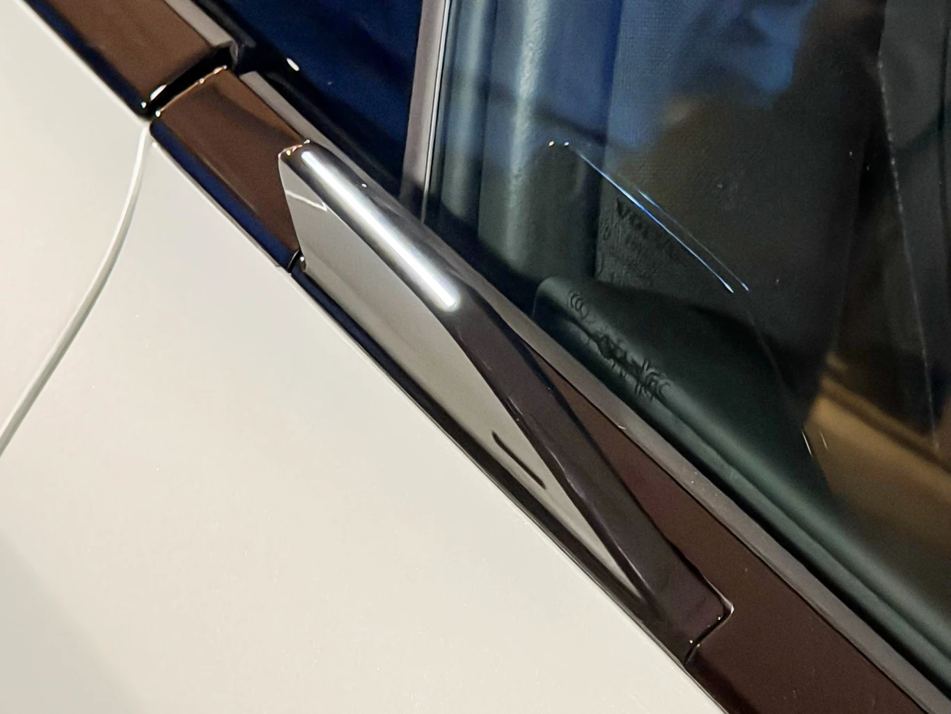 Fragment przedniej szyby samochodu z wyraźnie widocznym nowoczesnym wycieraczem oraz fragmentem białej karoserii.