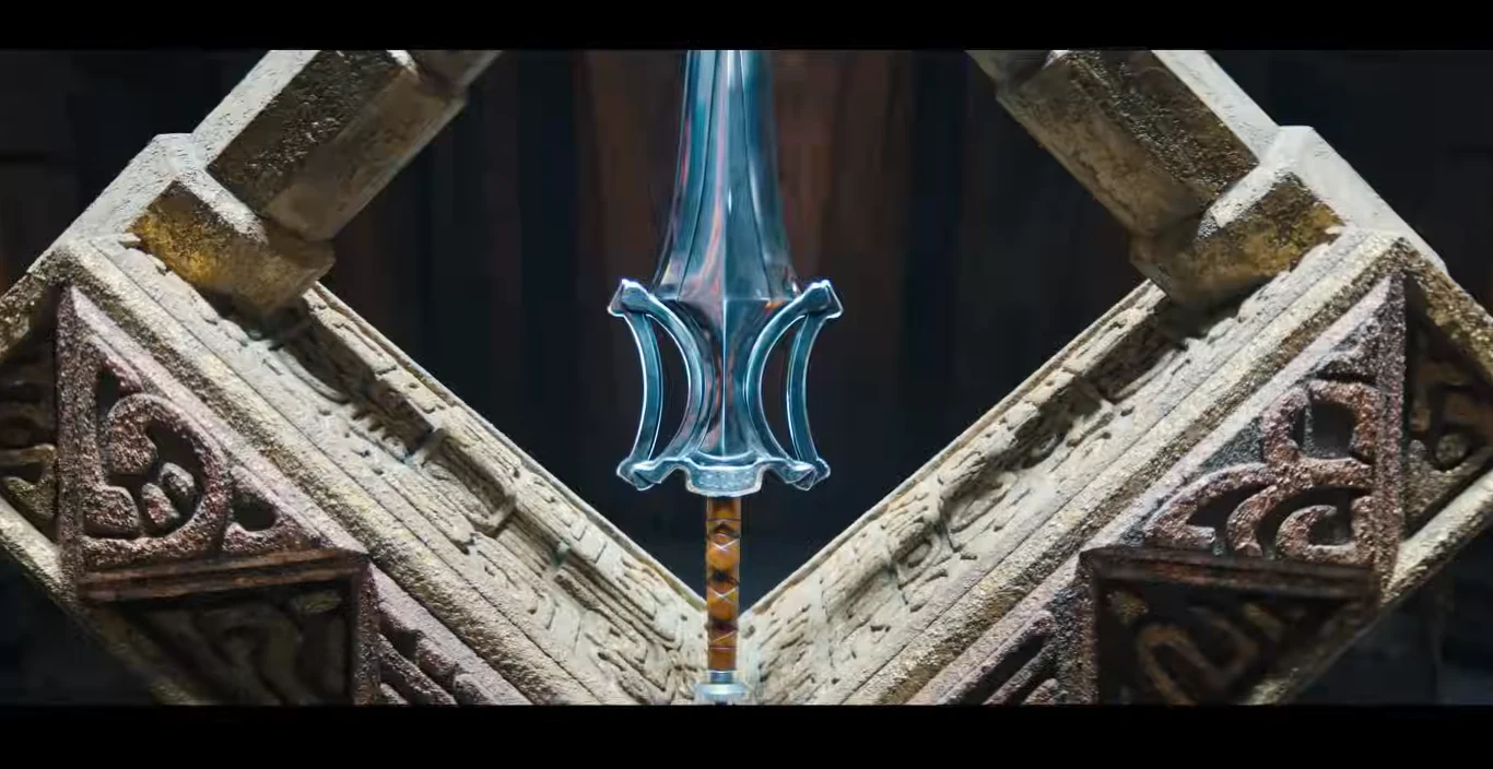 Kadr z zapowiedzi "Master of The Universe" Fantazyjny miecz o niebieskim ostrzu umieszczony centralnie, oparty o monumentalne, kamienne struktury z wyrytymi ornamentami.